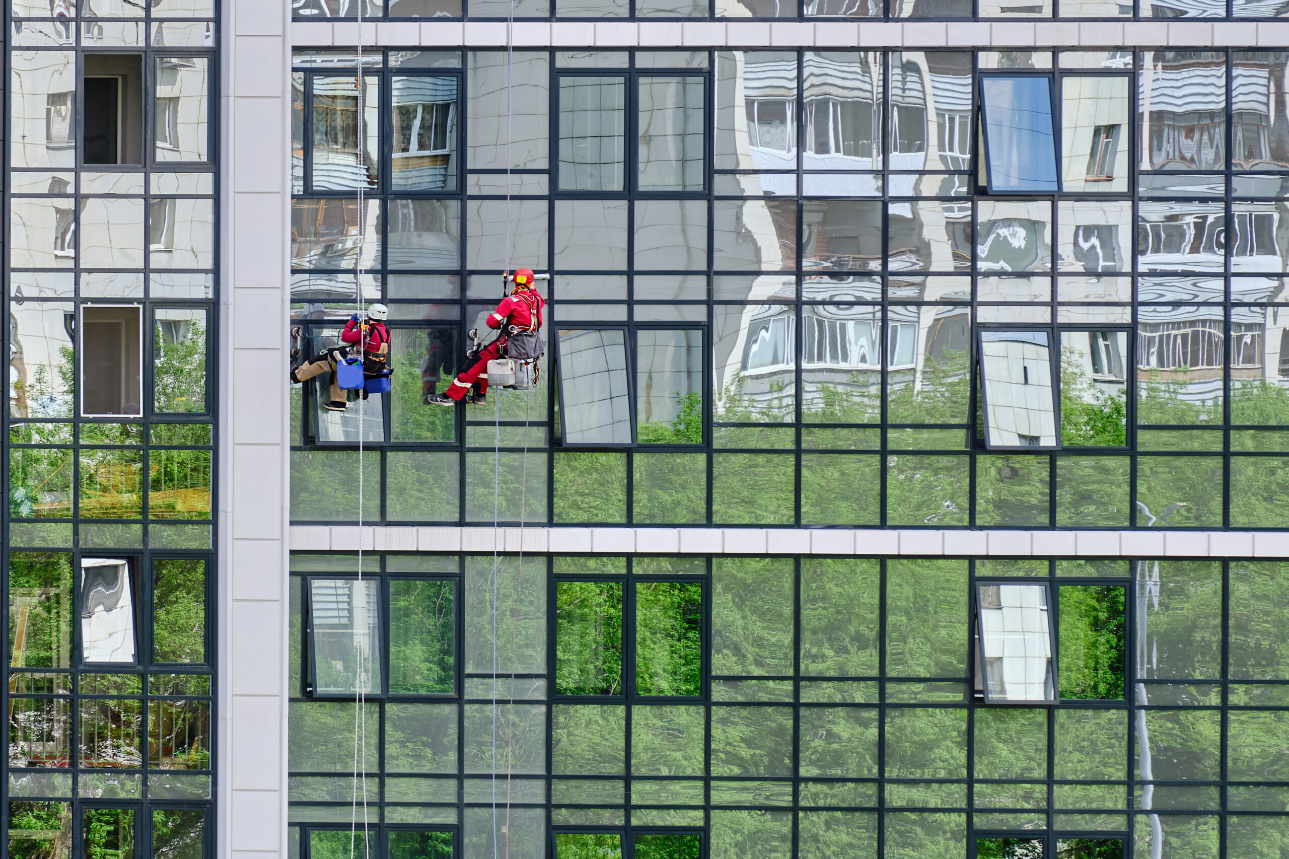Two industrial climbers from cleaning service wash glass facade of modern high-rise apartment building. Two industrial climbers from the cleaning service wash the glass facade of a modern high-rise apartment building. Rope access
